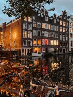 several bicycles parked on the side of a river next to buildings with lights in them