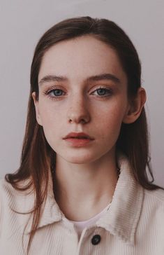 a young woman with blue eyes and long hair is looking at the camera while wearing a white shirt