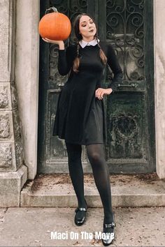 a woman in black dress holding an orange pumpkin