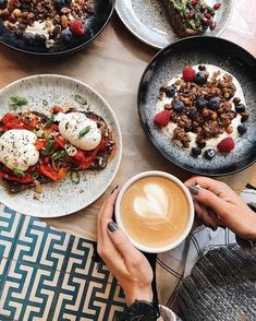 a person holding a cup of coffee in front of some plates with food on them