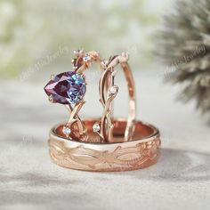 two gold rings with blue and white stones on them sitting next to a pine cone