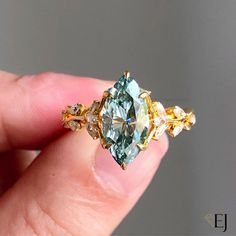 a person holding a ring with an aqua and yellow diamond in it's middle