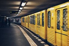 a yellow train traveling down tracks next to a loading platform at a subway station with people standing on the platform