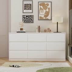 a white dresser sitting in a living room next to a lamp and pictures on the wall