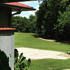 a red roof on top of a building next to a lush green field and trees