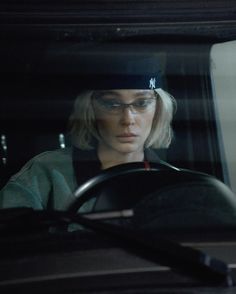 a woman wearing glasses sitting in the driver's seat of a car at night