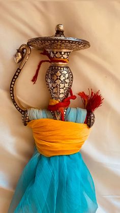 a decorative vase sitting on top of a white bed covered in blue and yellow fabric