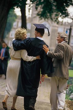 two people hugging each other in graduation gowns and cap, while others look on