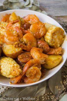 a white bowl filled with shrimp, corn and potatoes on top of a wooden table