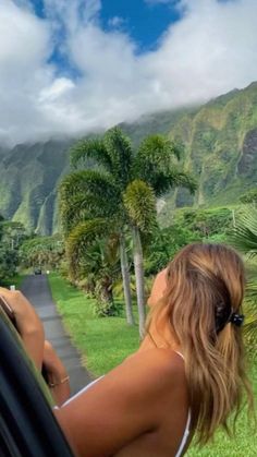 a woman leaning out the window of a car with mountains in the back ground and palm trees behind her