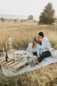 a man and woman are sitting on a blanket in the middle of an open field