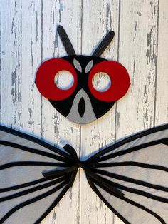 two masks with black and red wings on white wood planks, one is shaped like a bat