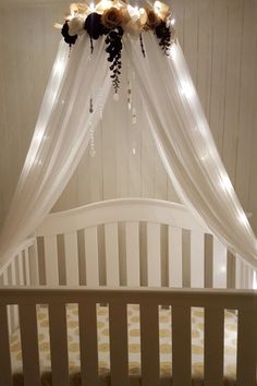 a white crib with flowers hanging from it's sides and lights on the ceiling