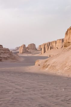 a man riding a horse in the desert with sand dunes and cliffs behind him on a cloudy day