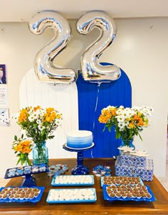 a table topped with cakes and desserts covered in blue icing next to balloons