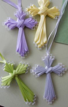 four different colored crosses hanging from strings on a white tablecloth with green and yellow ribbons