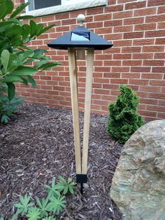 a wooden post with a solar panel on top in front of a brick wall and shrubbery