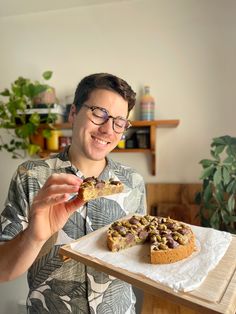 a man holding a piece of cake on top of a wooden tray next to a plant