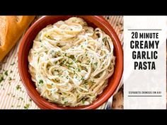 a red bowl filled with pasta and topped with parsley next to a loaf of bread