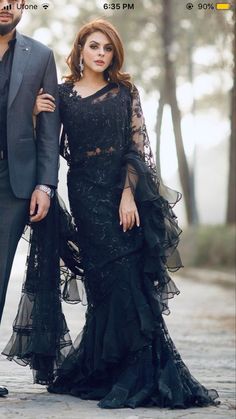 a man and woman in formal wear standing next to each other on a road with trees behind them