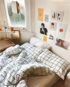 an unmade bed in a bedroom with pictures on the wall and window above it