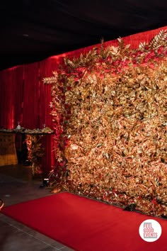 a red carpeted area with a large wall covered in gold leaves and plants on it