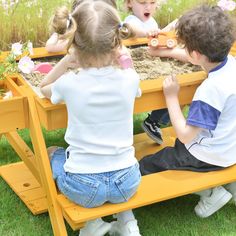 three children playing in a sandbox on the grass with their hands over the table