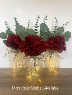 three vases with red flowers and greenery in them sitting on a wooden table