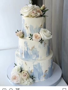 a three tiered cake with white and blue flowers on the top, sitting on a table