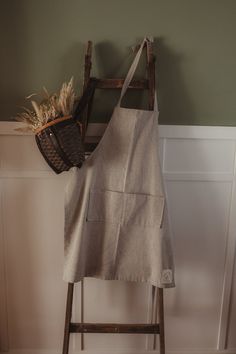 an apron hanging on a wooden ladder next to a basket with some plants in it