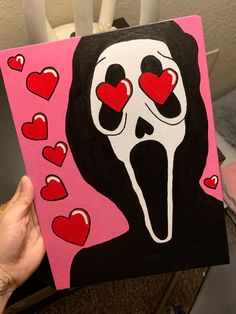 a person holding up a painting that looks like a scream face with hearts on it