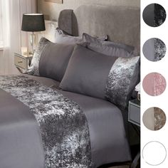 a bed with grey and silver comforters in a bedroom next to a night stand