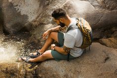 a man sitting on top of a rock next to a river