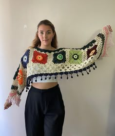 a woman standing in front of a white wall wearing a crocheted shawl