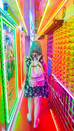 a woman walking down a hallway with neon lights on the walls and in front of her is a backpack