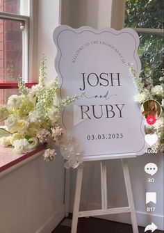 a white sign sitting in front of a window next to a vase with flowers on it