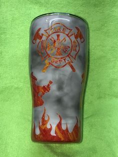 a glass cup with fire and flames painted on the side is sitting on a green cloth