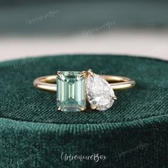 an emerald and diamond engagement ring sitting on top of a green velvet cushion