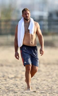 a shirtless man walking on the beach with a towel around his neck and head