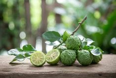 limes are arranged on a wooden table in front of green leaves and trees,