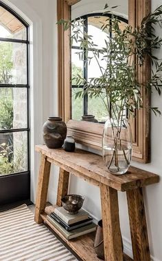 a wooden table topped with a vase filled with flowers next to a mirror and window