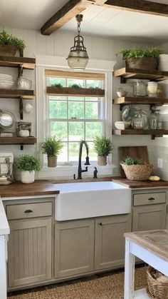 a kitchen filled with lots of open shelving next to a sink and window covered in potted plants