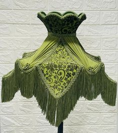 a green dress with fringes on it sitting on top of a wooden stand in front of a white brick wall