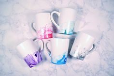 five coffee mugs with different colors and shapes on a marble counter top, one is blue, the other is pink