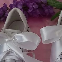 two pairs of shoes with white bows on them and purple flowers in the back ground