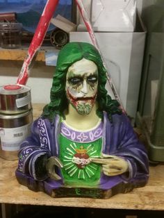 a statue of the joker is sitting on a table next to a paintbrush and some cans