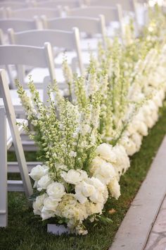 white flowers and greenery are lined up along the side of rows of chairs at an outdoor ceremony