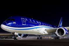 a large blue and white jetliner sitting on top of an airport tarmac at night