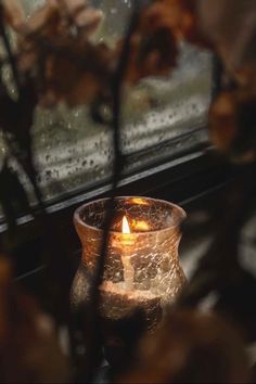 a lit candle sitting in front of a window sill with water droplets on it