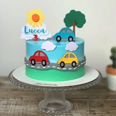 a blue cake with cars on it sitting on top of a table next to a potted plant